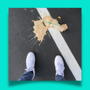 photo of legs and feet of person who is looking down at a spilled drink on the asphalt